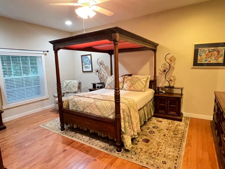 A bedroom with a canopy 4-poster bed, wood floors, a tapestry area rug, and wood nightstands and dresser.