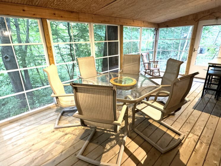 An outdoor screened in deck with an octagon shaped table and 6 chairs.