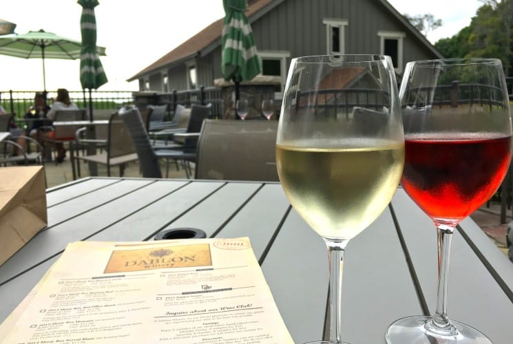 Glasses of red and white wine by a menu on an outdoor table at a restaurant