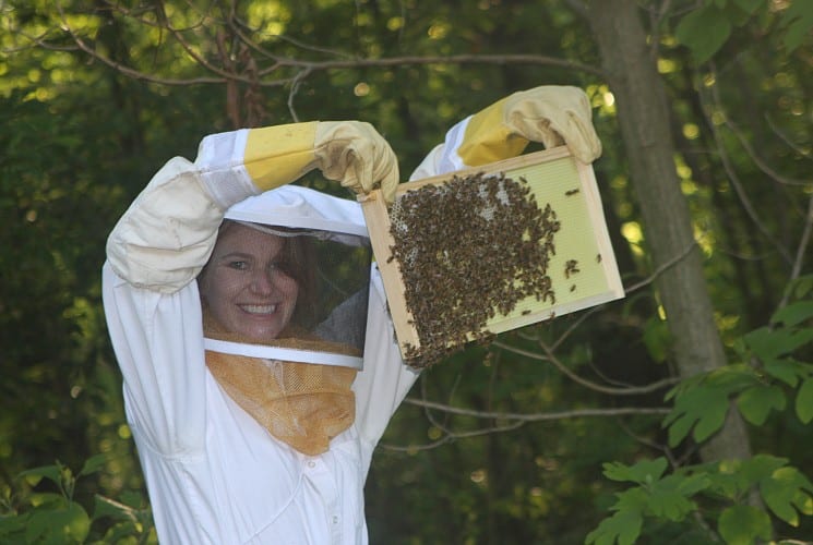 A woman in a white bee suit holding a rack full of bees