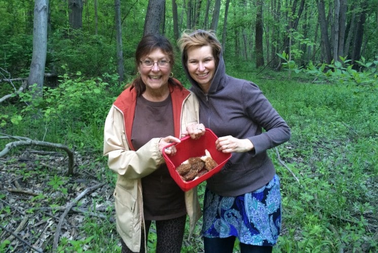 Two ladies in the woods holding a bucket as they forage for mushrooms