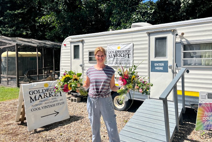 A woman holding two bouquets of flowers outside a white camper being used as a market