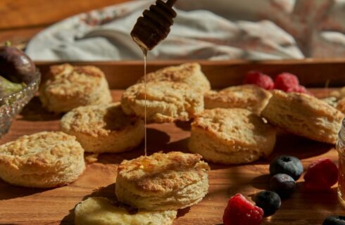 Honey being drizzled on a platter full of freshly baked biscuits and berries