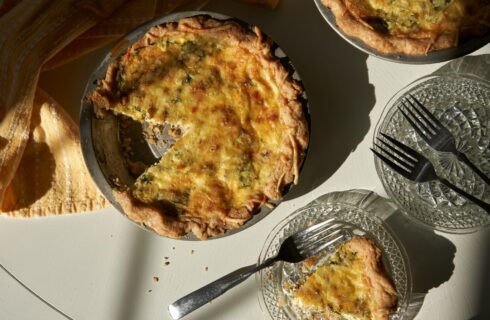 Pie plate of a freshly baked quiche with a slice and fork on a glass plate