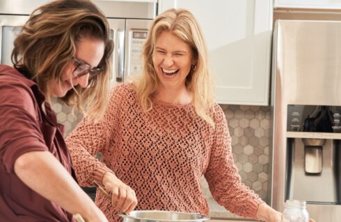 Two women laughing together as they bake in a kitchen