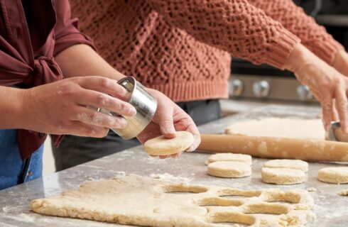 Two women cutting out biscuits from freshly prepared dough on a kitchen counter