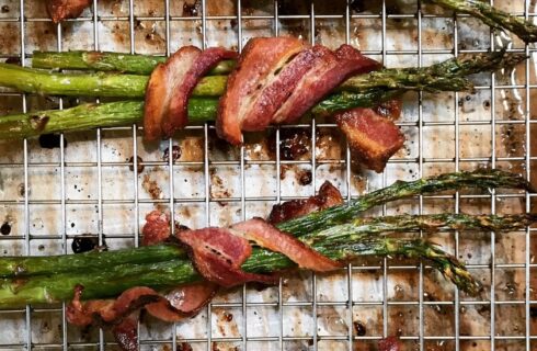 Wire cooling rack with two bundles of asparagus wrapped in bacon