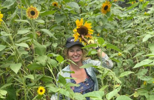 A woman in a baseball cap standing in a patch of tall sunflowers