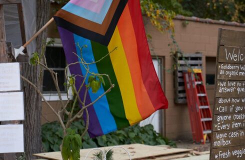 A rainbow flag hanging by a brown welcome sign