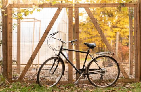 A black bicycle standing next to a wooden gate in the woods