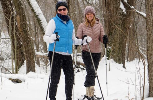 Two ladies snowshoeing through the woods during winter