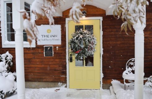 The yellow front door of a home with a hanging wreath and welcome sign during wintertime
