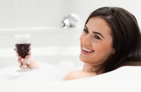 A woman holding a glass of red wine while sitting in a jacuzzi bath full of bubbles