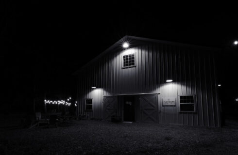 Nighttime view of a white barn with three lights on and string lights in a side yard