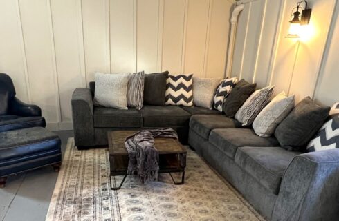 Lounging area with a grey sectional couch with patterned pillows and a leather chair and ottoman