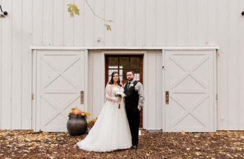 A bride and groom standing in front of large barn doors of a white barn