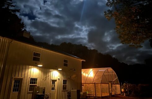 A large white barn next to a covered outdoor pool with cloudy night skies above
