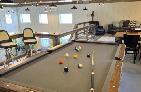 Loft area of a large white barn with a pool table and sitting area with couch and tables and chairs