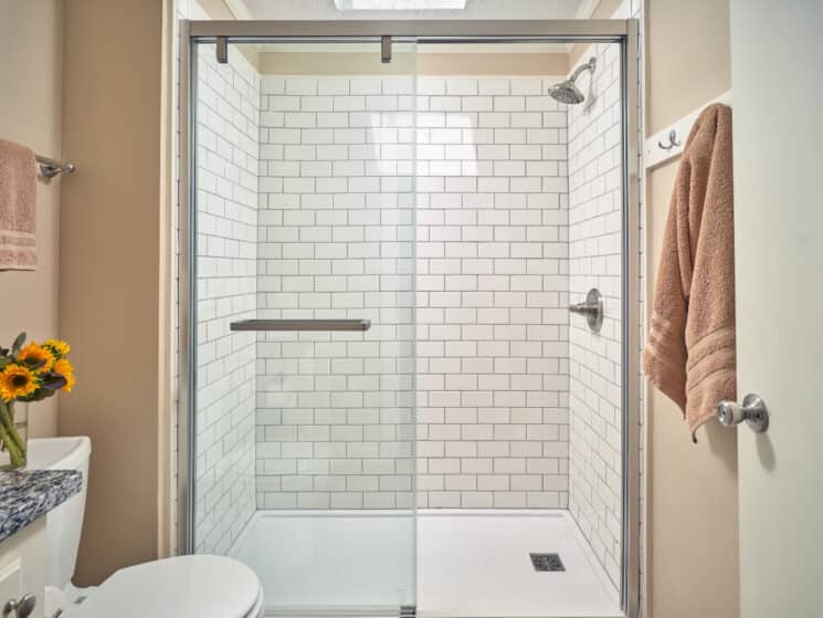A bathroom with a walk in shower with white tiled walls and stainless steel fixtures.