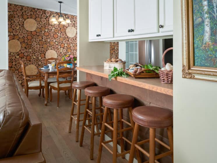 Kitchen with white cabinets, leather stools underneath a long countertop, a wood dining table, and the back of a leather sofa