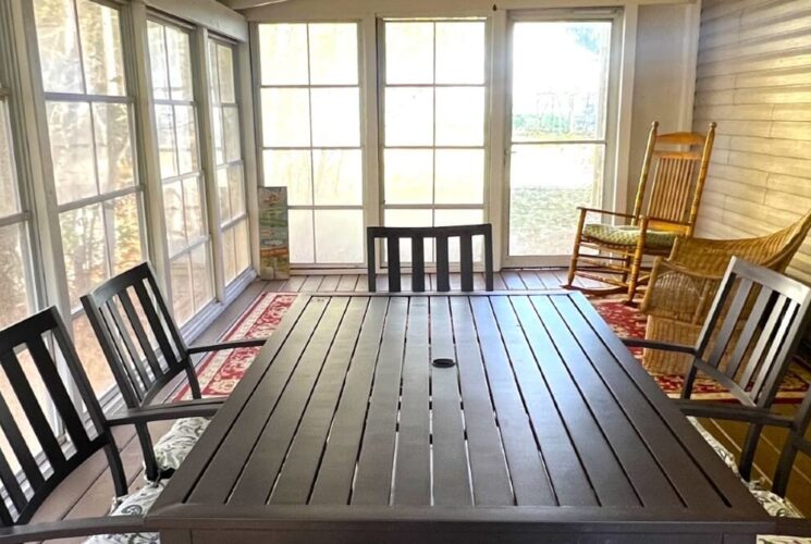 Outdoor screened in porch with black table and chairs, buffet hutch and two rocking chairs