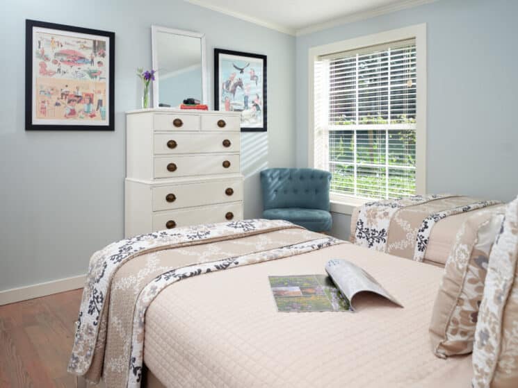 Small bedroom with two twin beds, tall white dresser, and blue chair by a window