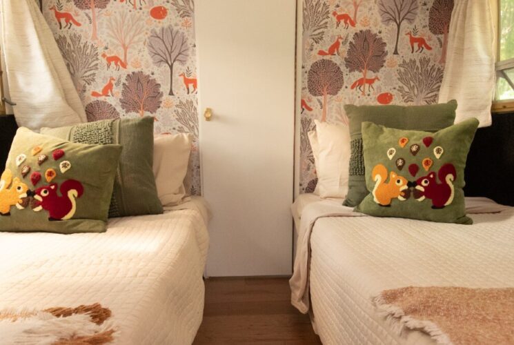 Two small twin beds in a camper with floral wallpaper and windows