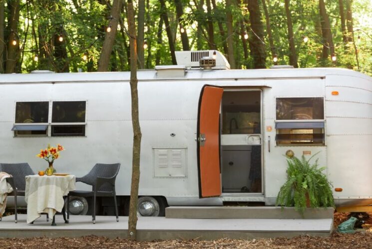 Vintage airstream camper nestled in the woods with a concrete pati, table and two chairs