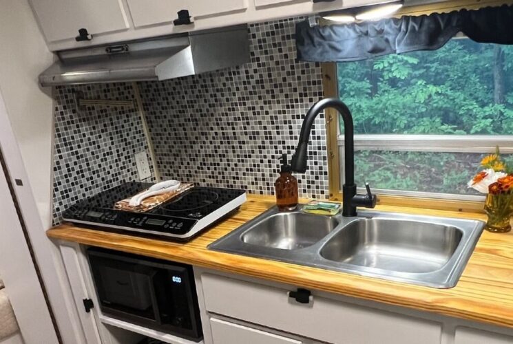 Kitchen in a camper with sink, wood counter, silver fan, window and tiled backsplash