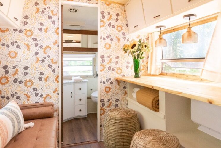 Inside of an aistream camper decorated in soft neutral colors with couch, long wood counter and doorway into a bathroom