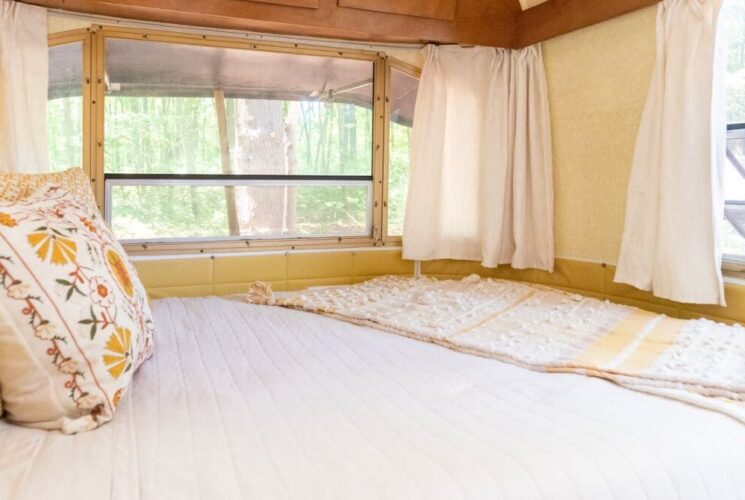 Queen bed with yellow and white quilt and pillows in an airstream camper with lots of windows