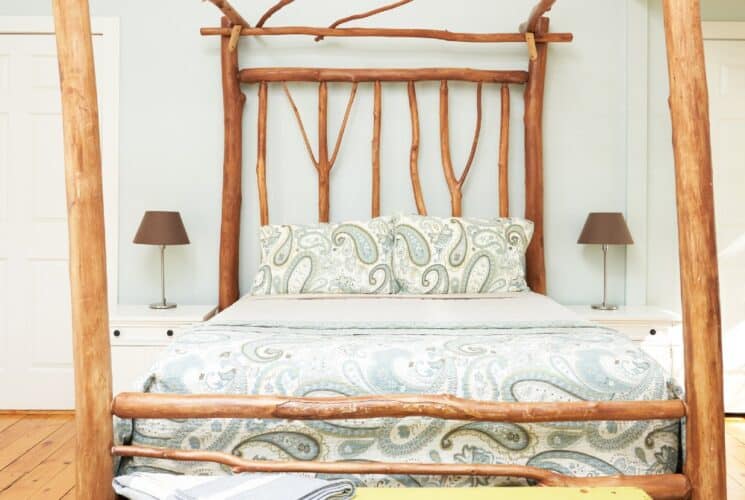 A bright bedroom featuring a bed frame made of ironwood with a paisley comforter and pillows and two side tables with lamps