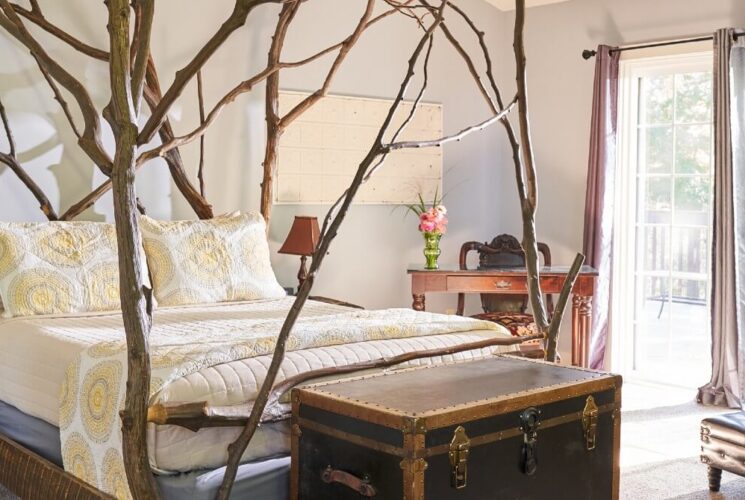 Spacious, bright bedroom with a custom queen sized bed with branch detail, leather chair, desk and slider doors to a patio