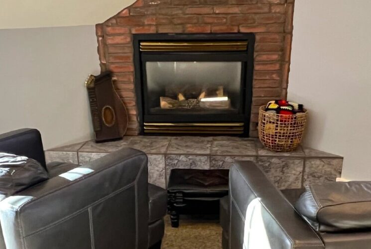 Two black plush leather chairs facing a cozy corner gas fireplace