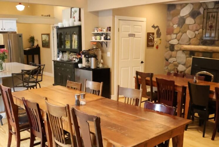 Spacious kitchen with two long wood tables wit eight chairs each in front of a large stone fireplace
