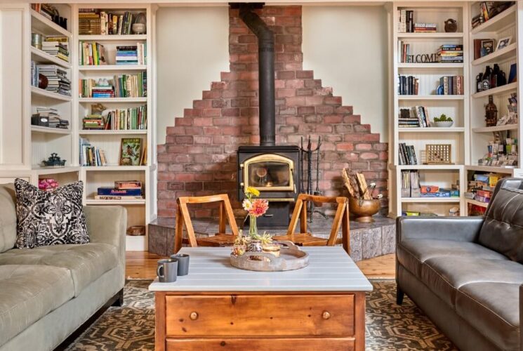 Bright living room with two couches, coffee table, pipe fireplace flanked by built in bookshelves