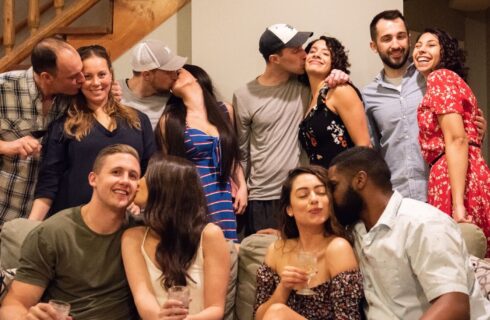 A group of six couples gathered together, each one giving their significant other a kiss