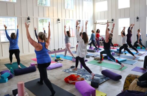 A group of women doing yoga in a large white barn full of bright windows