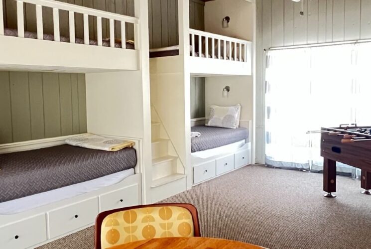 Large room with four built in white bunk beds, foosball table by large slider doors