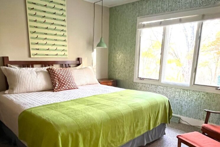 Cozy bedroom in hues of green with queen bed, sitting chair and large windows