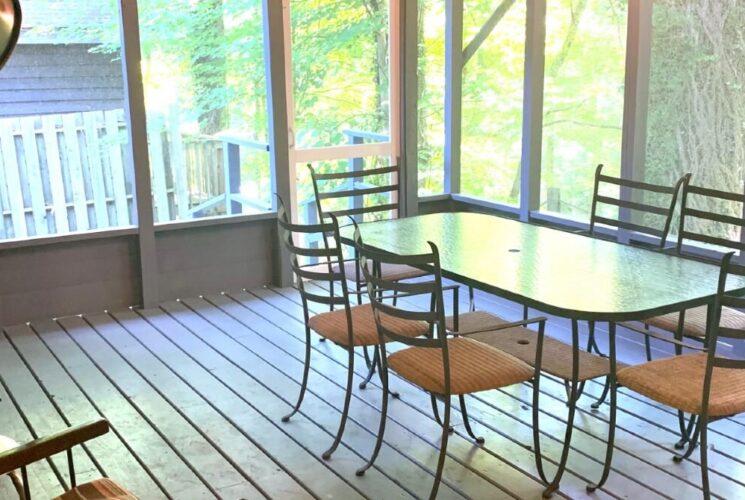 Outdoor screened in porch with a table and six chairs overlooking a wooded area