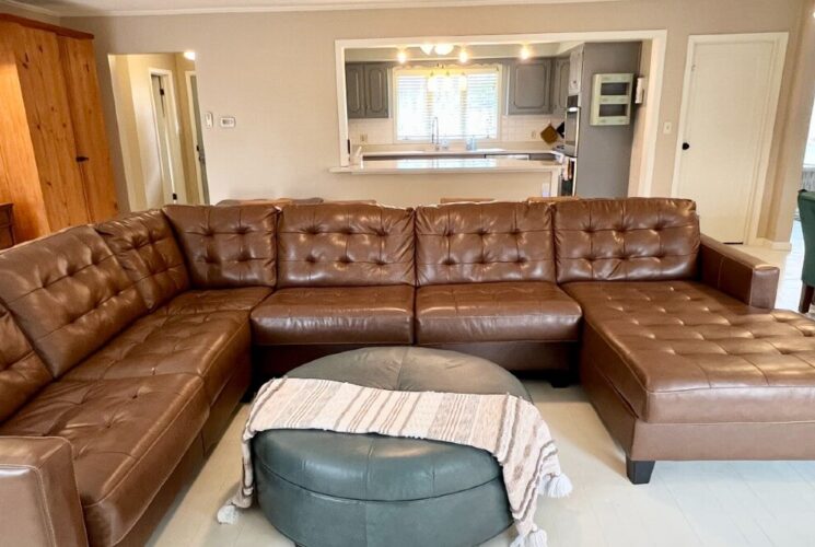 Living room with large brown leather sectional in front of a kitchen