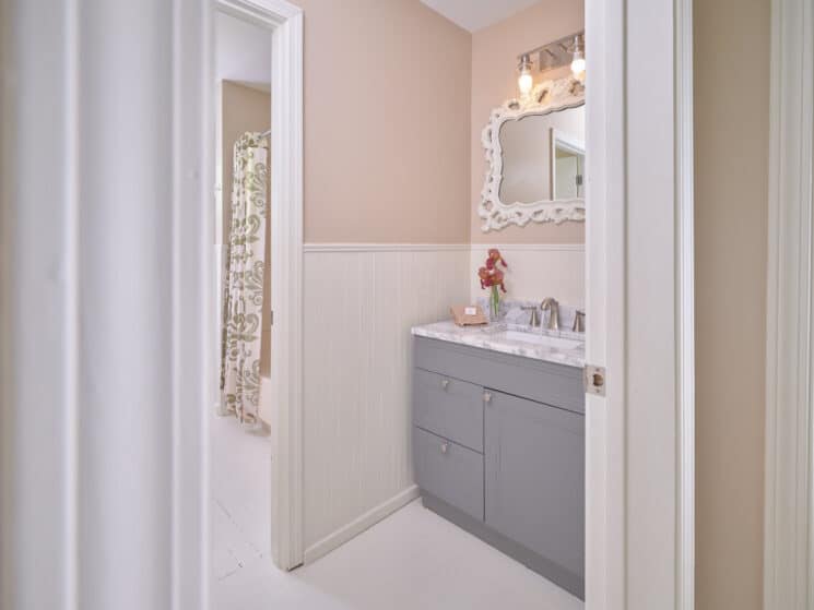 A bathroom with a grey vanity with granite countertop with single sink, and a white framed mirror above it.