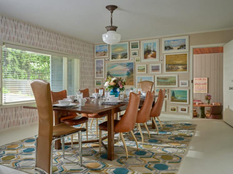 Eclectic dining room with long table and 12 chairs, colorful wallpaper and gallery wall full of framed pictures
