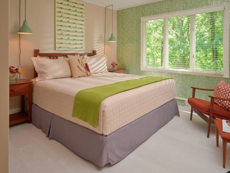 Cozy bedroom in hues of green with queen bed, sitting chair and large windows