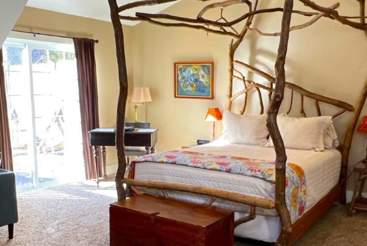 Elegant bedroom with a crooked four-poster bed made from sassafras, cathedral ceilings, carpeted floors and slider door to a patio.
