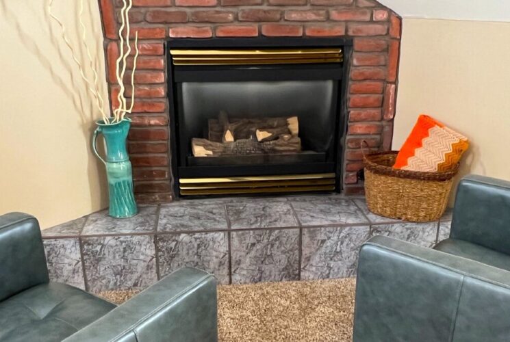 Two grey leather chairs in front of a corner gas fireplace with brick detail