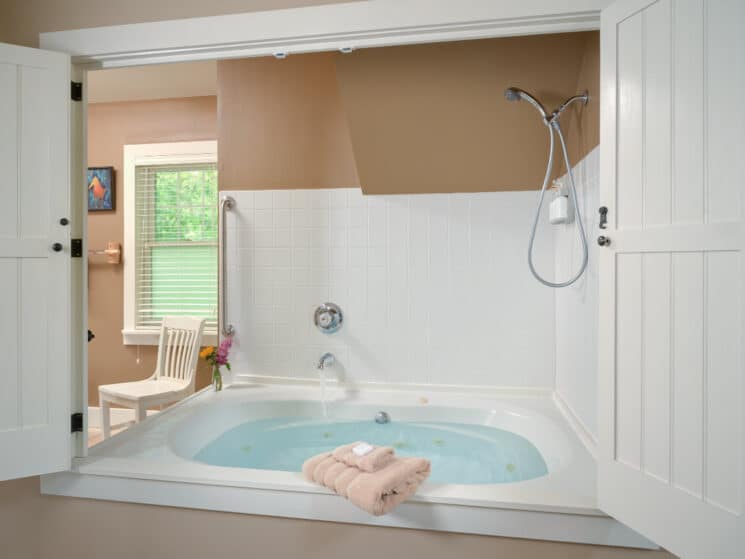 Large jacuzzi tub/shower combo with white tile and an open doorway into another room with a white chair