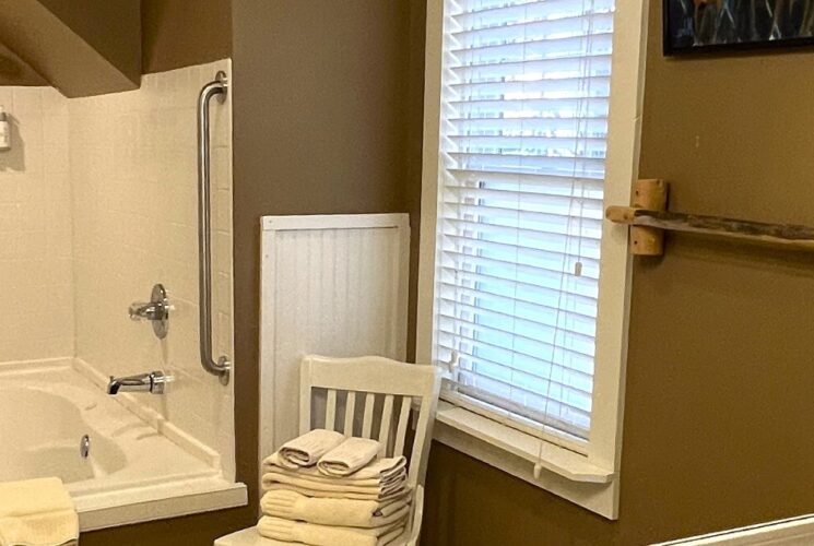 Shower with large mirror, soaker tub/shower and white chair by a window holding folded towels