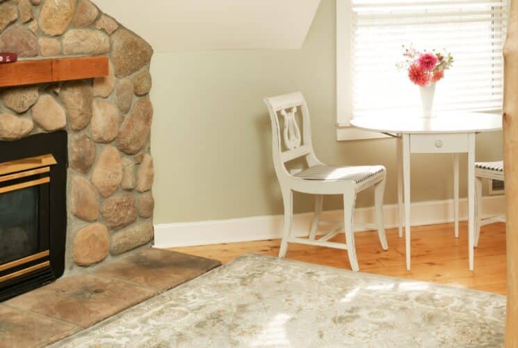 Small white desk and two chairs by a window and stone fireplace